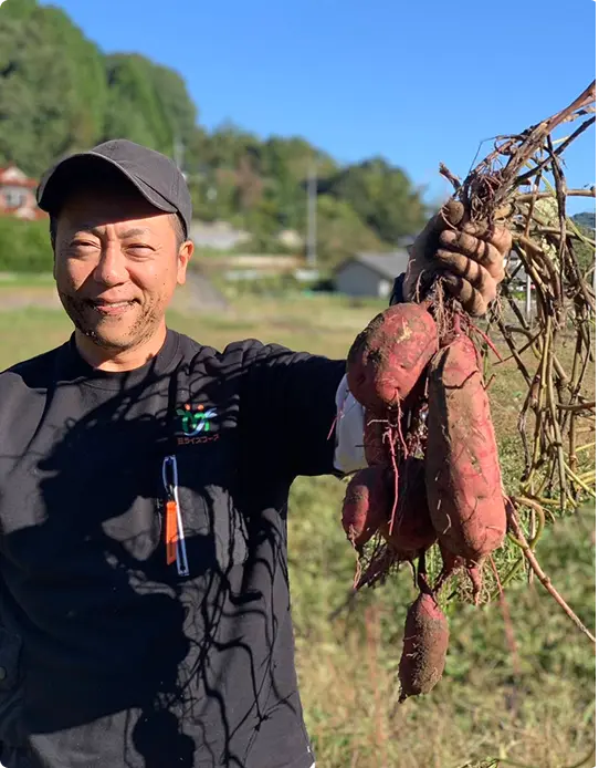 収穫したサツマイモを手にする生産者